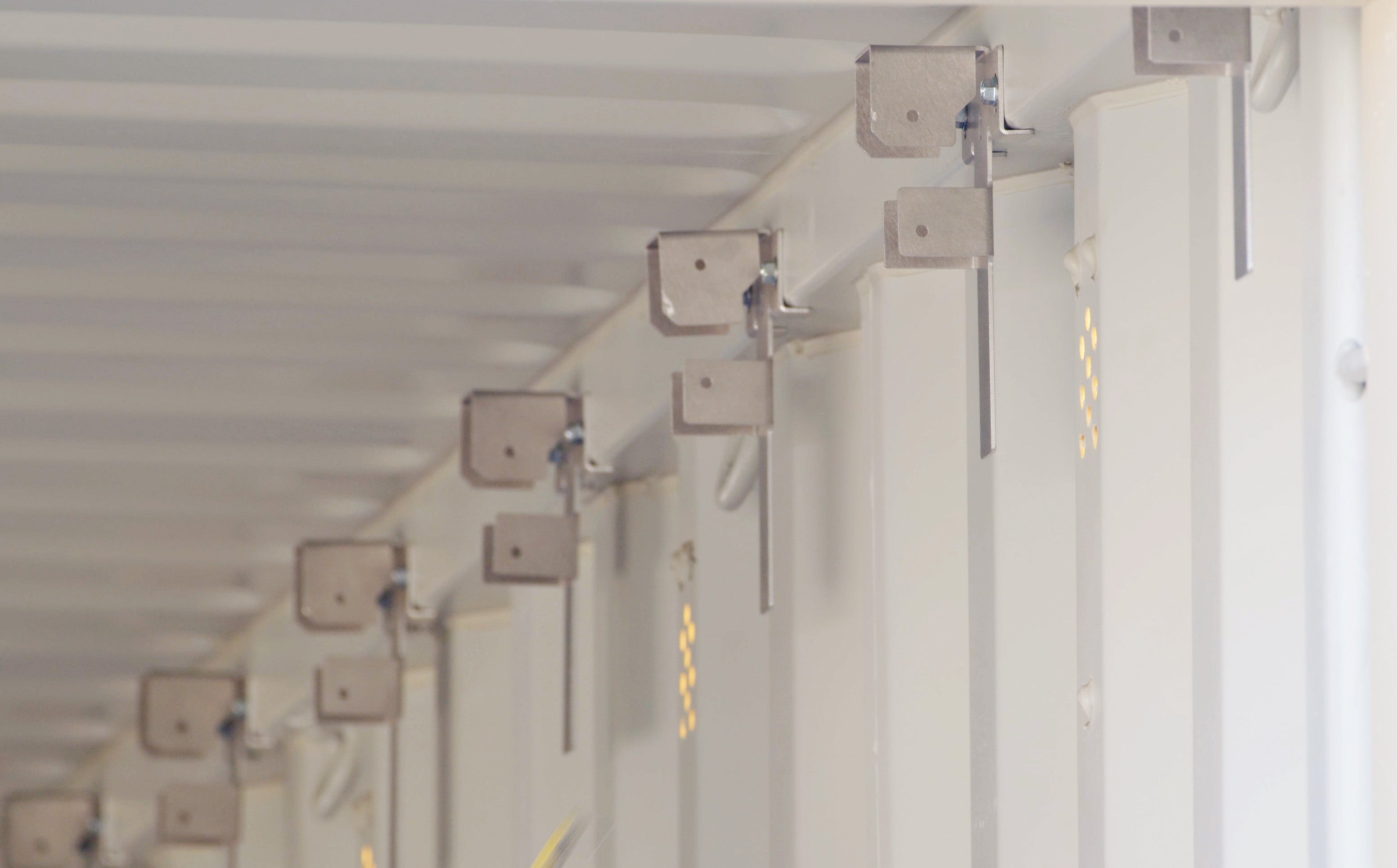 Row of aluminum interior wood stud brackets installed along the top tubing of a white shipping container for framing support