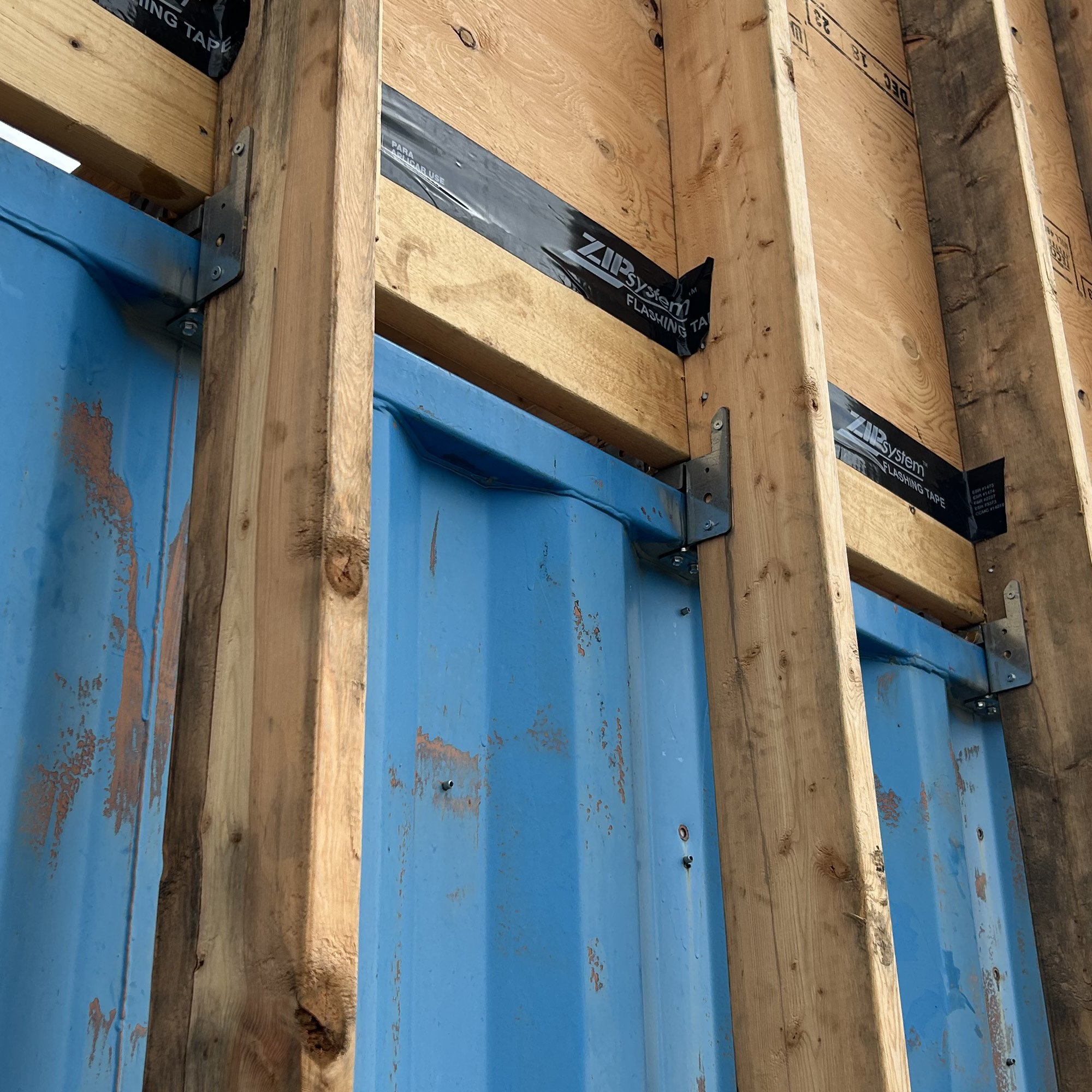 Exterior wood framing brackets mounted to blue shipping container using galvanized steel mounts for structural support