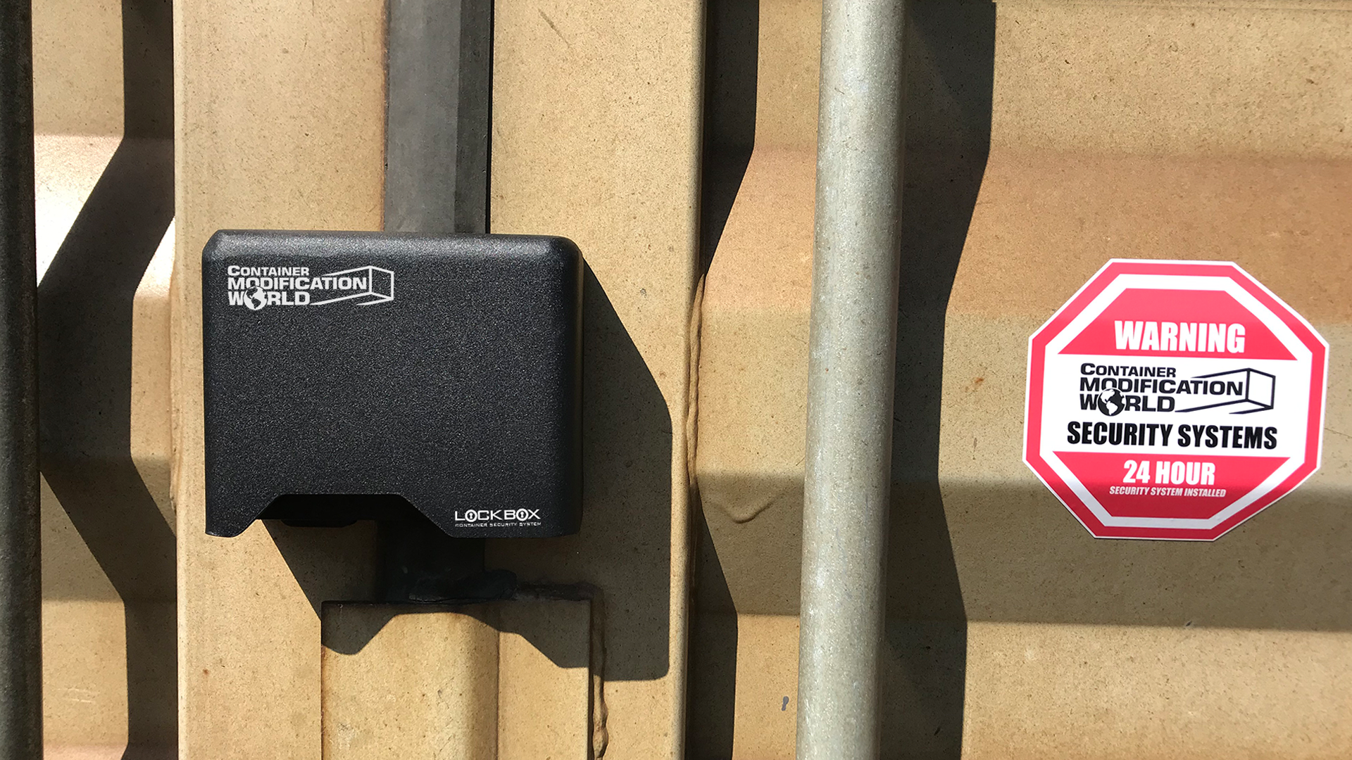 Installed Right Hand Container Lock Box from Container Modification World on a beige shipping container door, shown beside a red warning security sticker for 24-hour surveillance